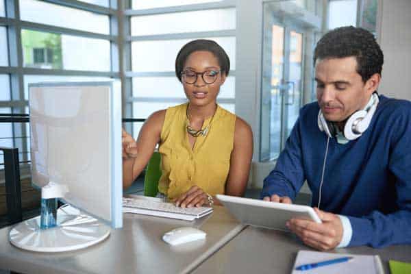 Two colleages discussing ideas using a tablet and computer